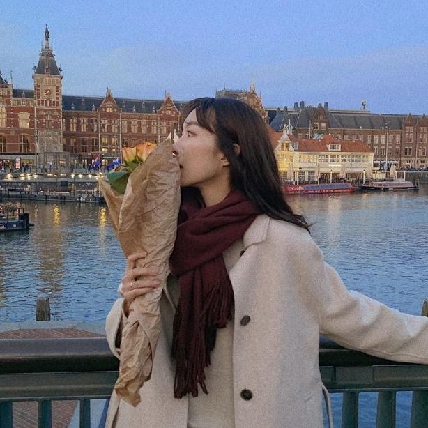 Jieun cozied up in a scarf and coat holding a bouquet to cover her face